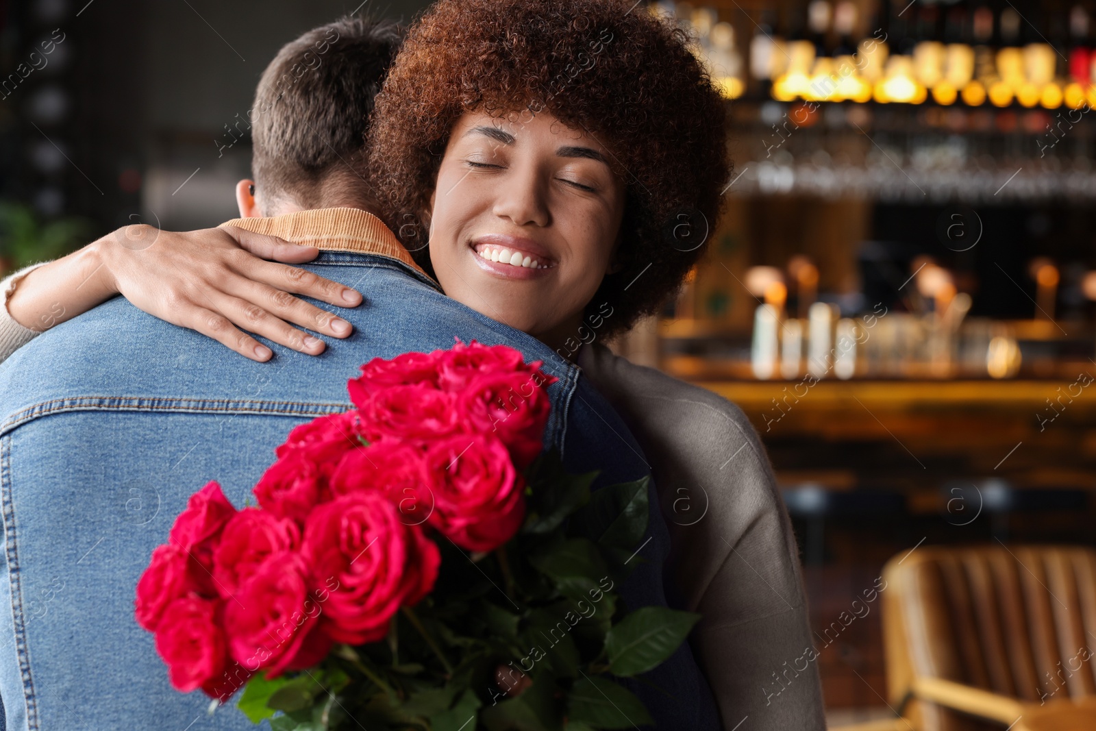 Photo of International dating. Beautiful woman with bouquet of roses hugging her boyfriend in cafe