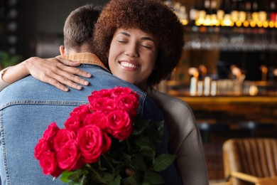 International dating. Beautiful woman with bouquet of roses hugging her boyfriend in cafe