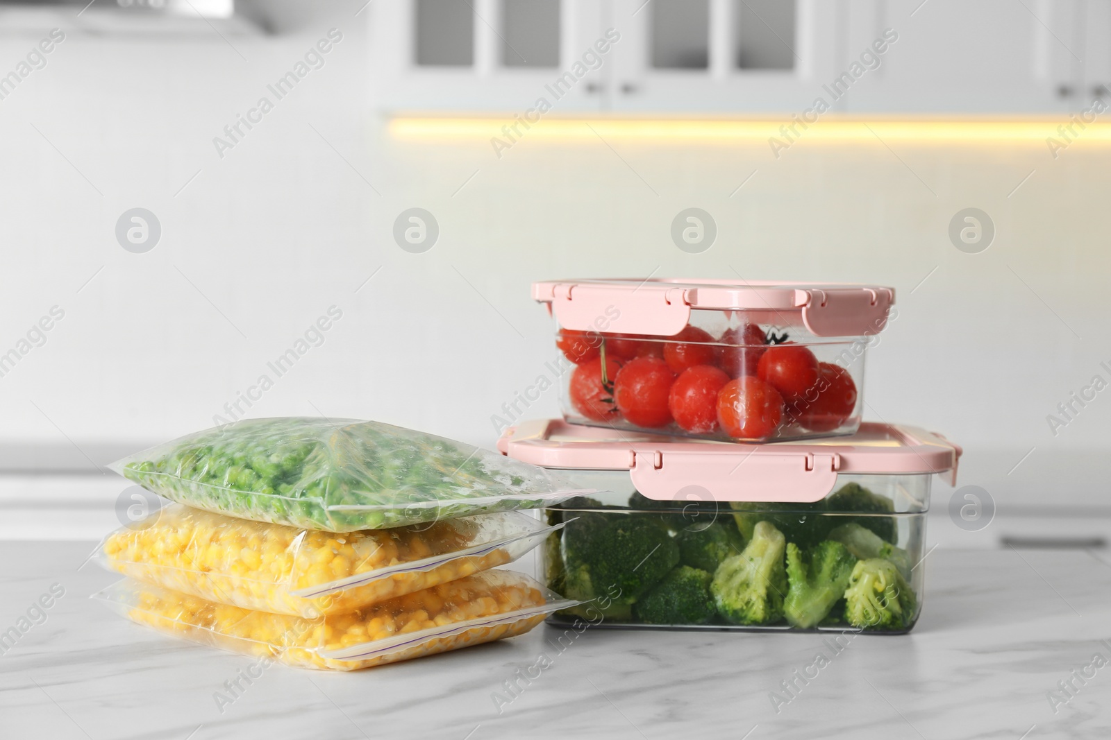 Photo of Plastic bags and containers with different frozen vegetables on white marble table in kitchen