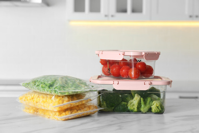 Plastic bags and containers with different frozen vegetables on white marble table in kitchen