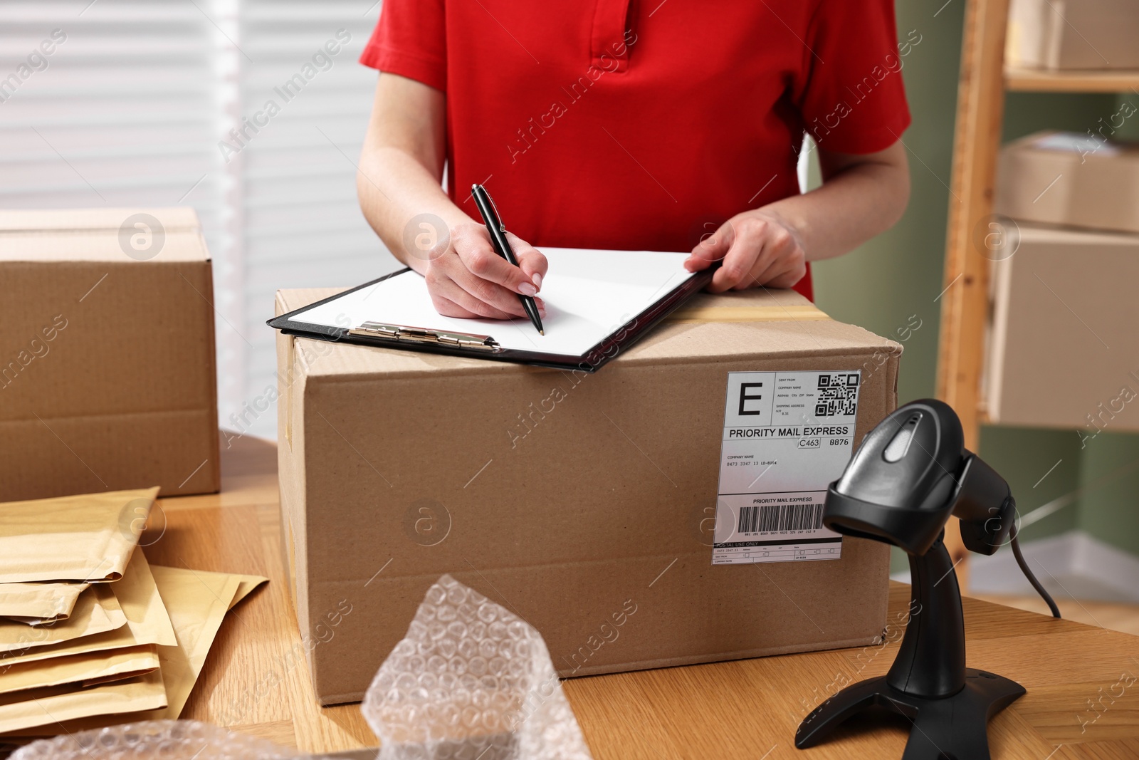 Photo of Parcel packing. Post office worker with clipboard and box at wooden table indoors, closeup