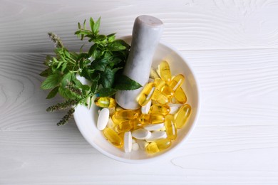 Photo of Mortar with fresh green herbs and pills on white wooden table, top view