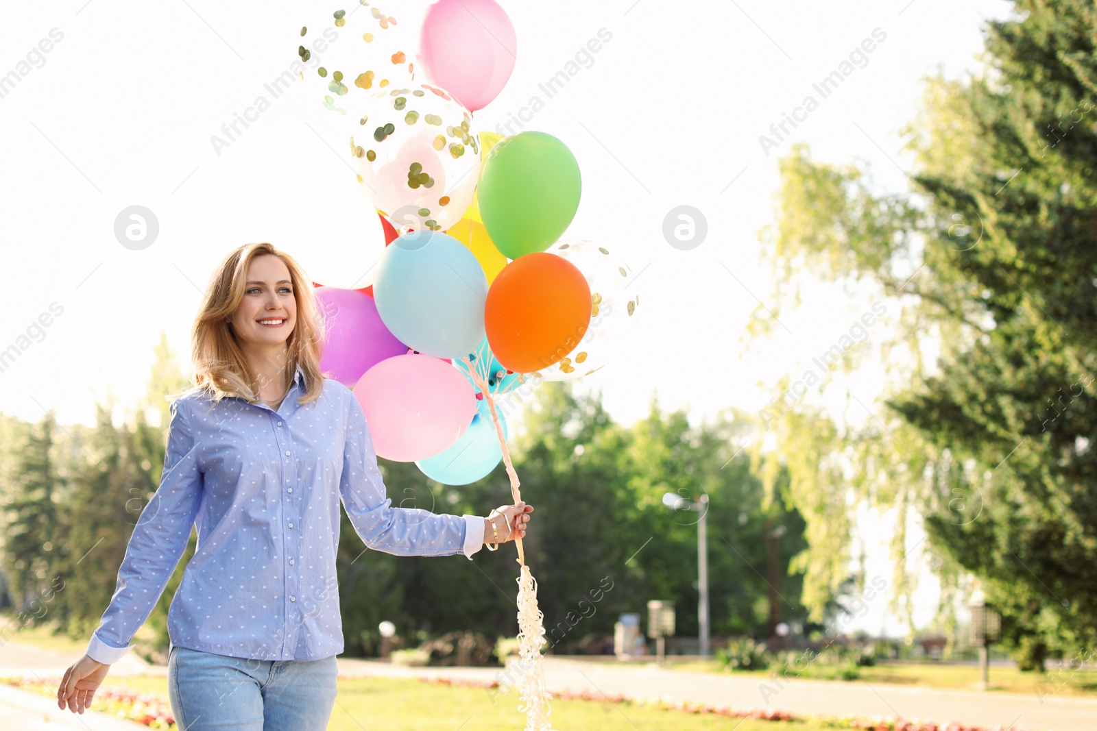 Photo of Young woman with colorful balloons outdoors on sunny day