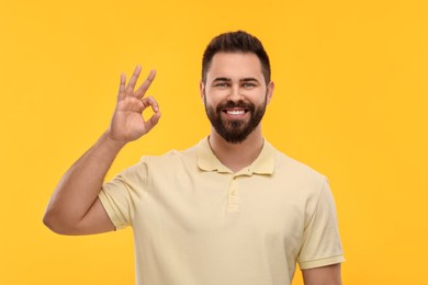 Photo of Man with clean teeth showing OK gesture on yellow background