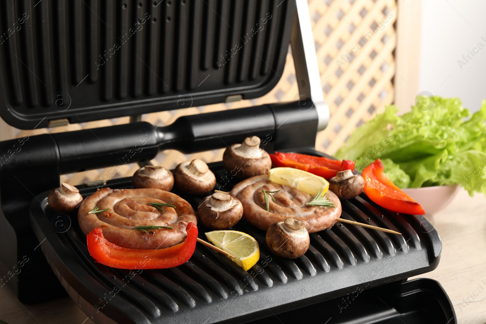 Photo of Electric grill with homemade sausages, bell pepper and mushrooms on table, closeup