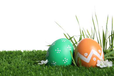 Photo of Colorful Easter eggs and flowers on green grass against white background, closeup