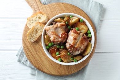 Photo of Tasty cooked rabbit with vegetables in bowl and bread on white wooden table, top view