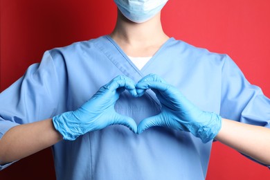 Photo of Doctor making heart with hands on red background, closeup