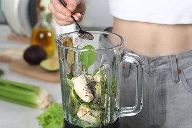 Photo of Woman adding chia seeds into blender with ingredients for green smoothie indoors, closeup