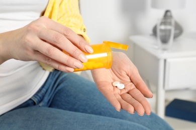 Photo of Woman pouring pills from bottle into hand indoors, closeup