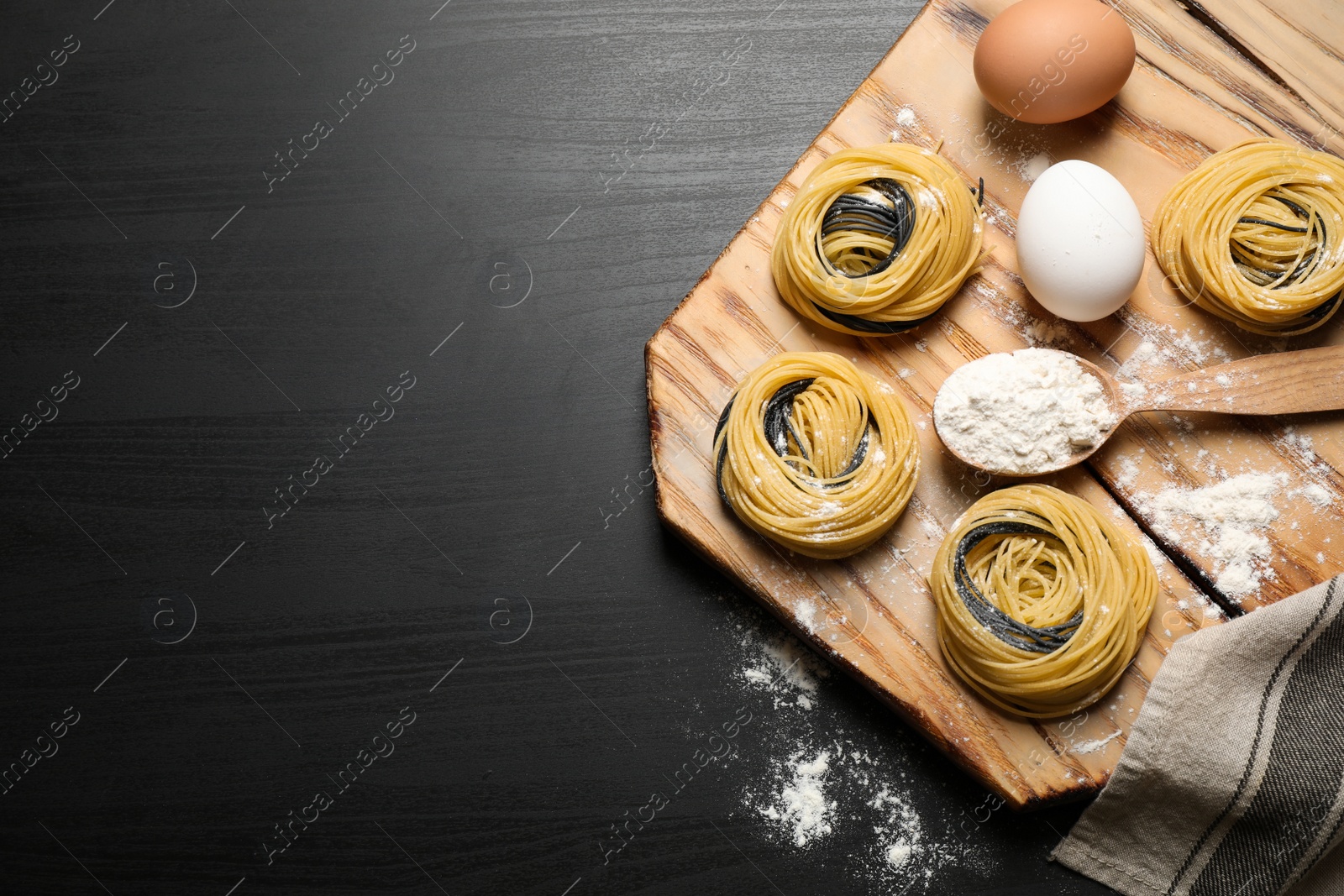 Photo of Raw linguine pasta and products on black wooden table, flat lay. Space for text