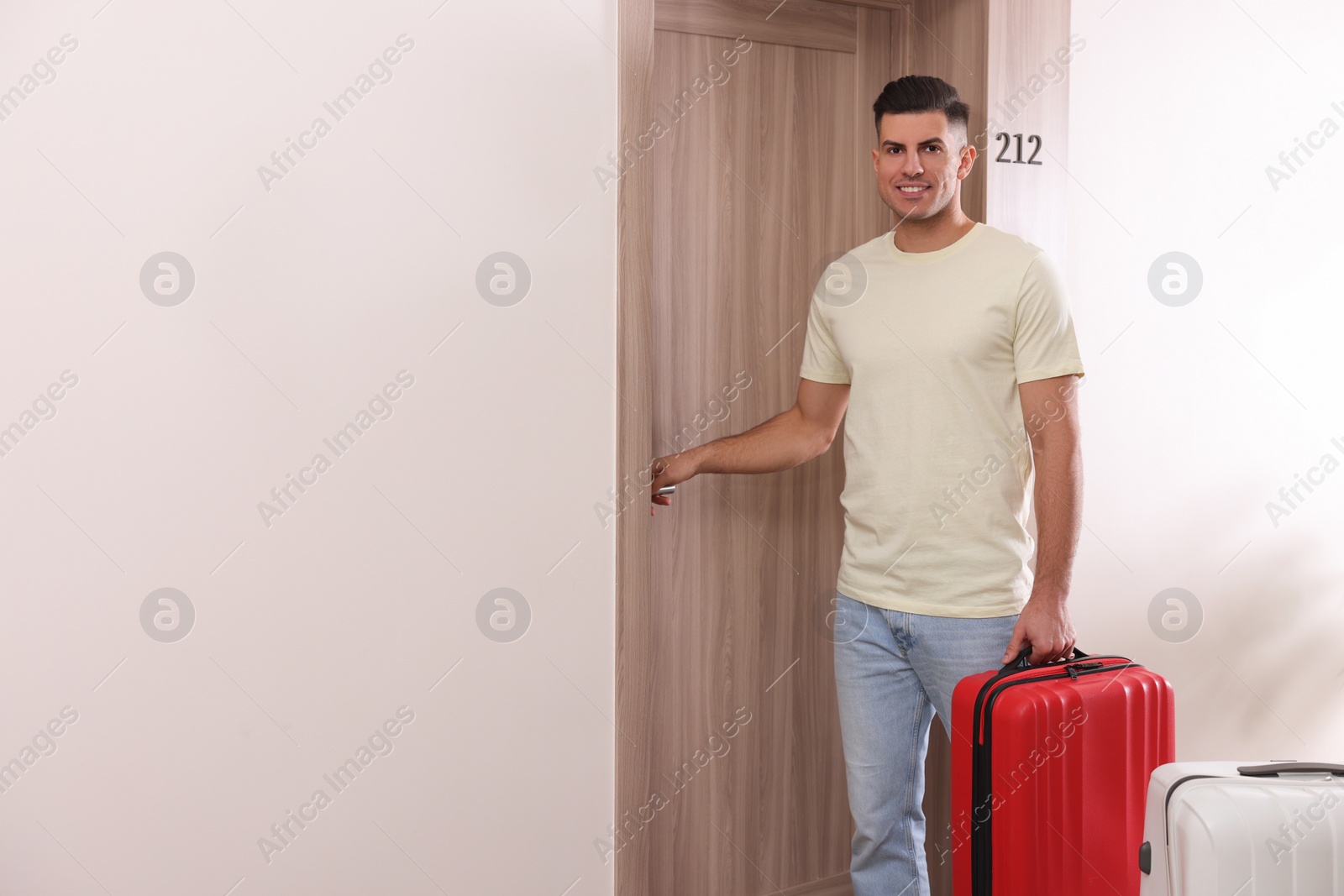 Photo of Happy man with suitcase opening door in hotel