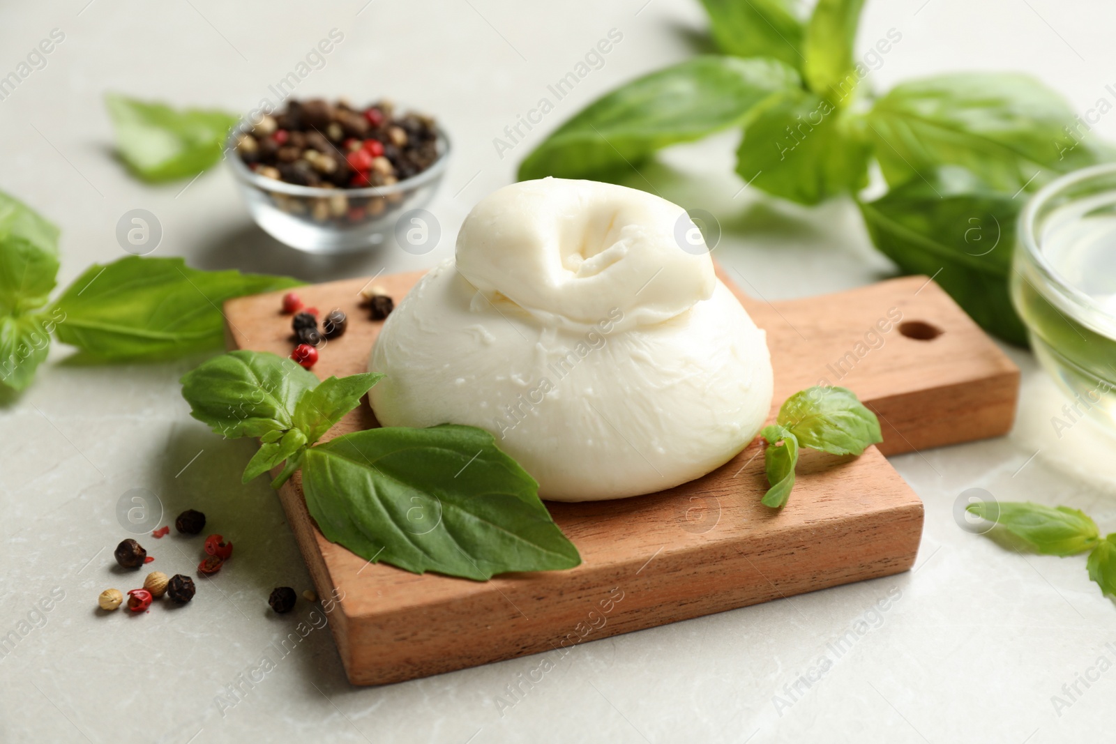 Photo of Delicious burrata cheese with basil and spices on light table, closeup