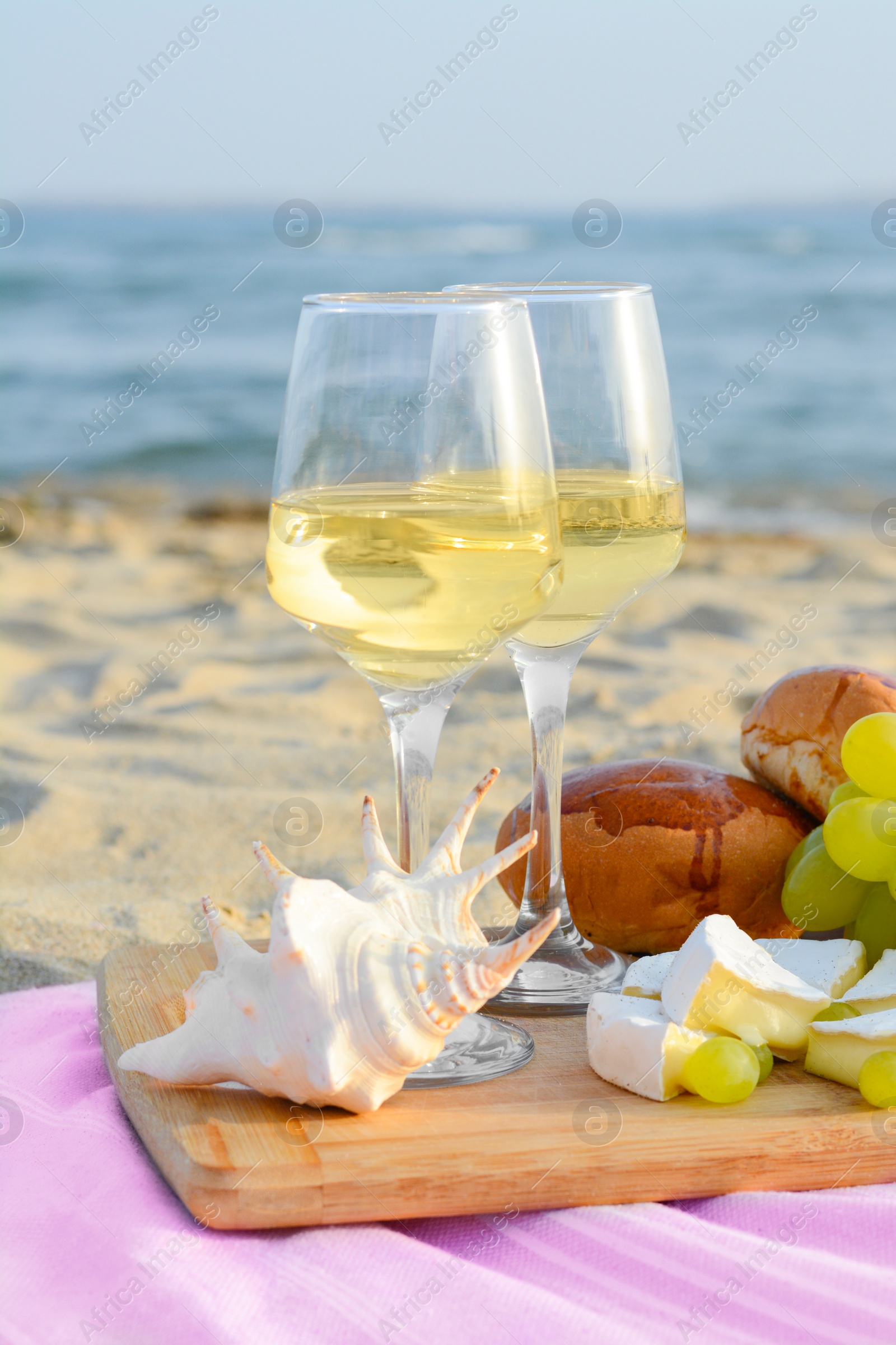 Photo of Glasses with white wine and snacks for beach picnic on sandy seashore