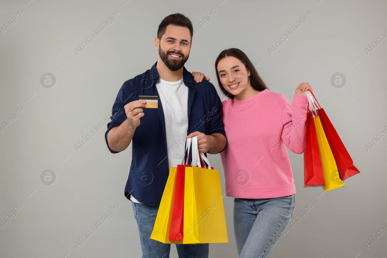 Photo of Happy couple with shopping bags and credit card on grey background