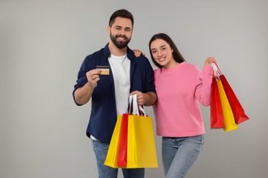 Happy couple with shopping bags and credit card on grey background