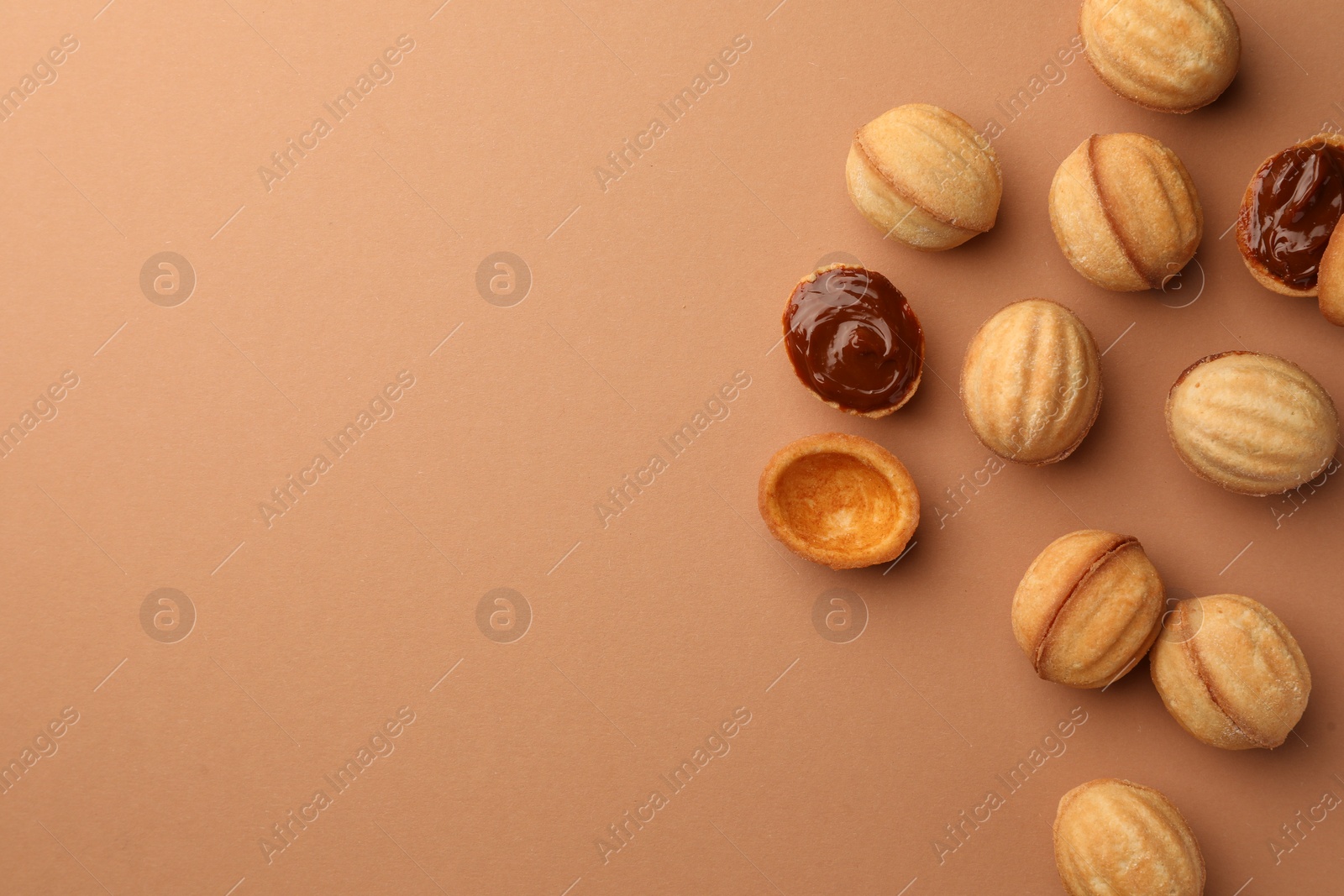 Photo of Homemade walnut shaped cookies with boiled condensed milk on pale brown background, flat lay. Space for text