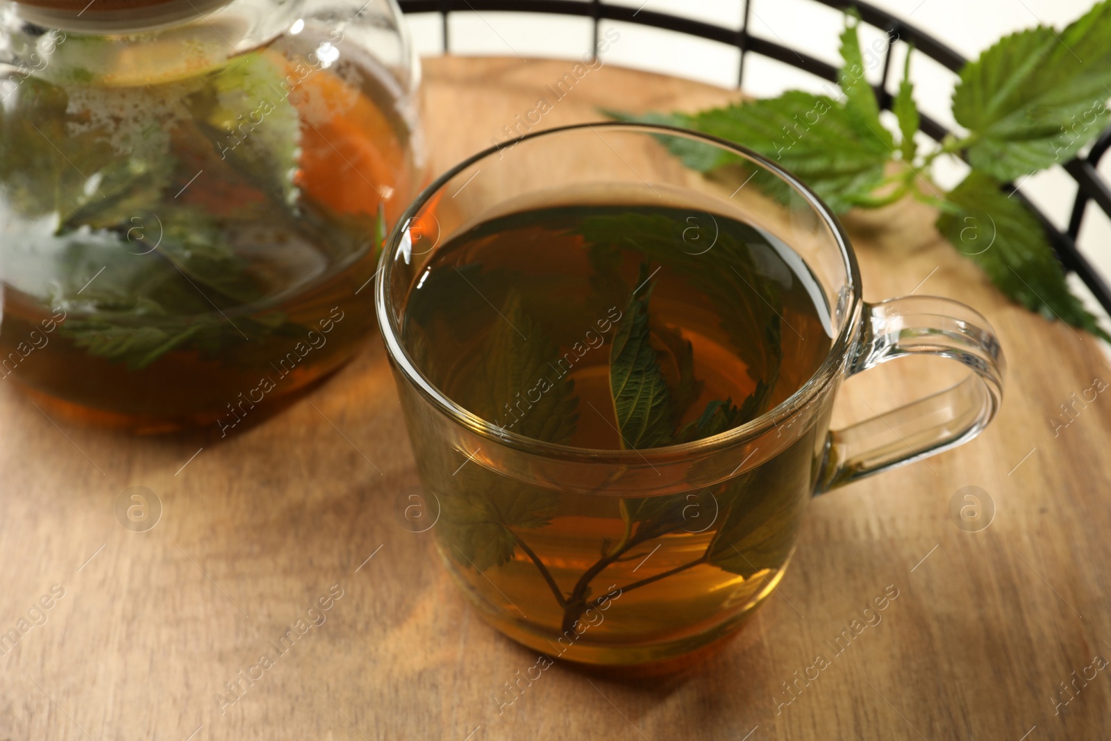 Photo of Aromatic nettle tea and green leaves on wooden tray, closeup