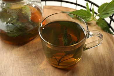 Aromatic nettle tea and green leaves on wooden tray, closeup