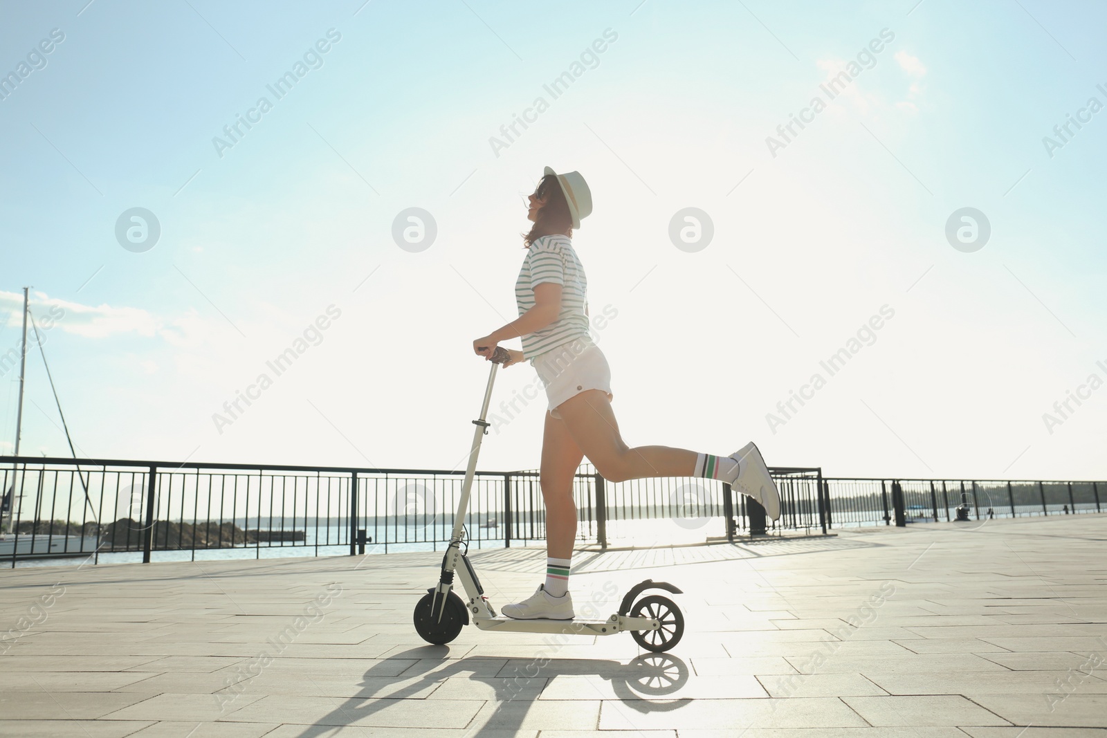 Photo of Young woman riding modern kick scooter along waterfront