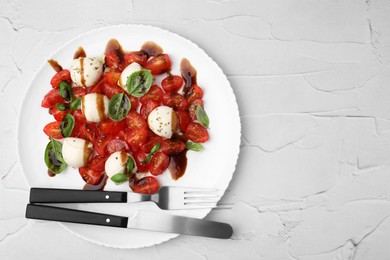 Photo of Tasty salad Caprese with tomatoes, mozzarella balls, basil and cutlery on white textured table, top view. Space for text