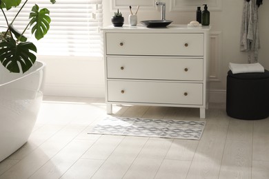 Stylish mat with pattern near chest of drawers in bathroom