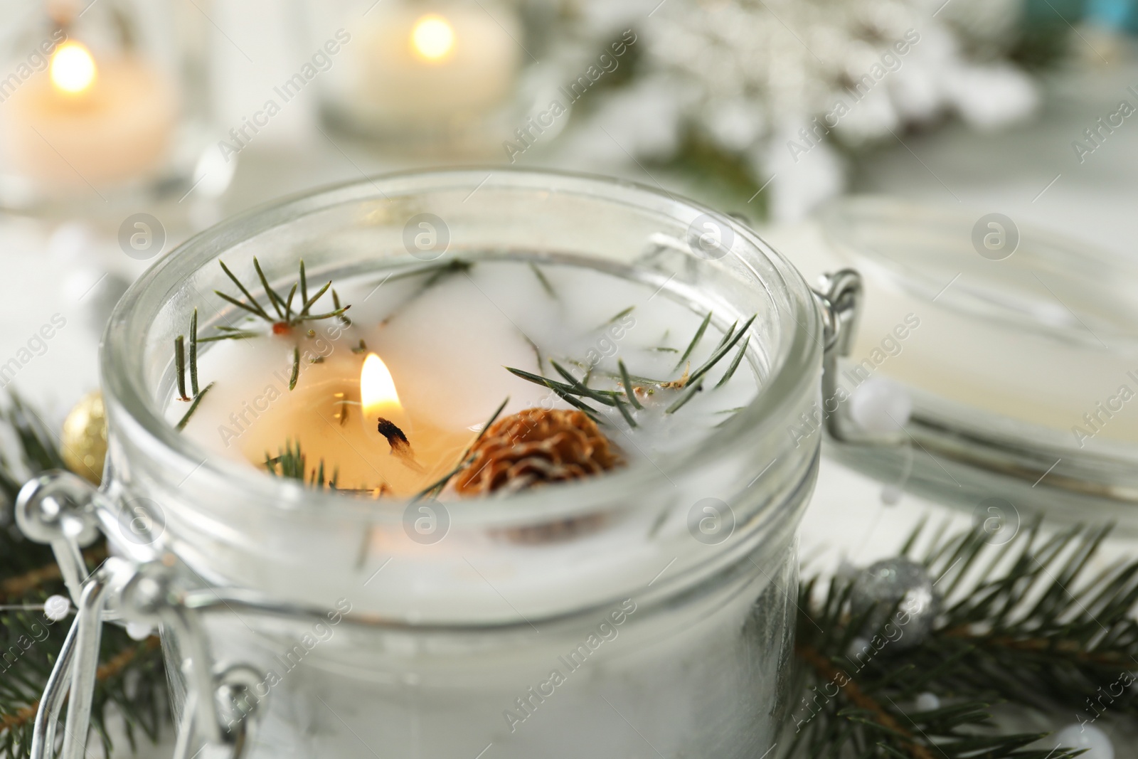 Photo of Burning scented conifer candle in glass jar, closeup view