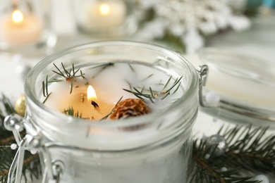 Burning scented conifer candle in glass jar, closeup view