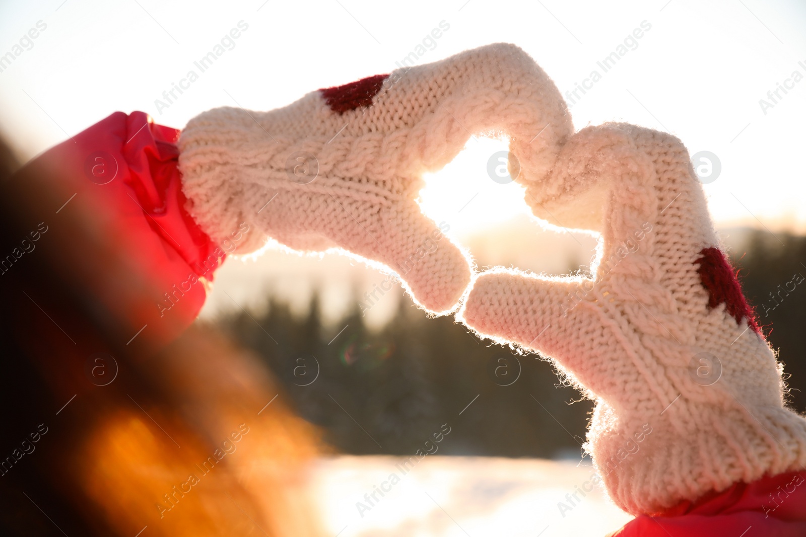 Photo of Woman making heart with hands outdoors at sunset, closeup. Winter vacation