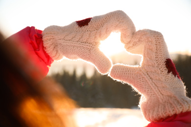 Photo of Woman making heart with hands outdoors at sunset, closeup. Winter vacation