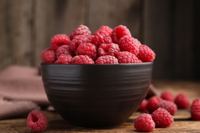 Bowl with fresh ripe raspberries on wooden table against blurred background, closeup