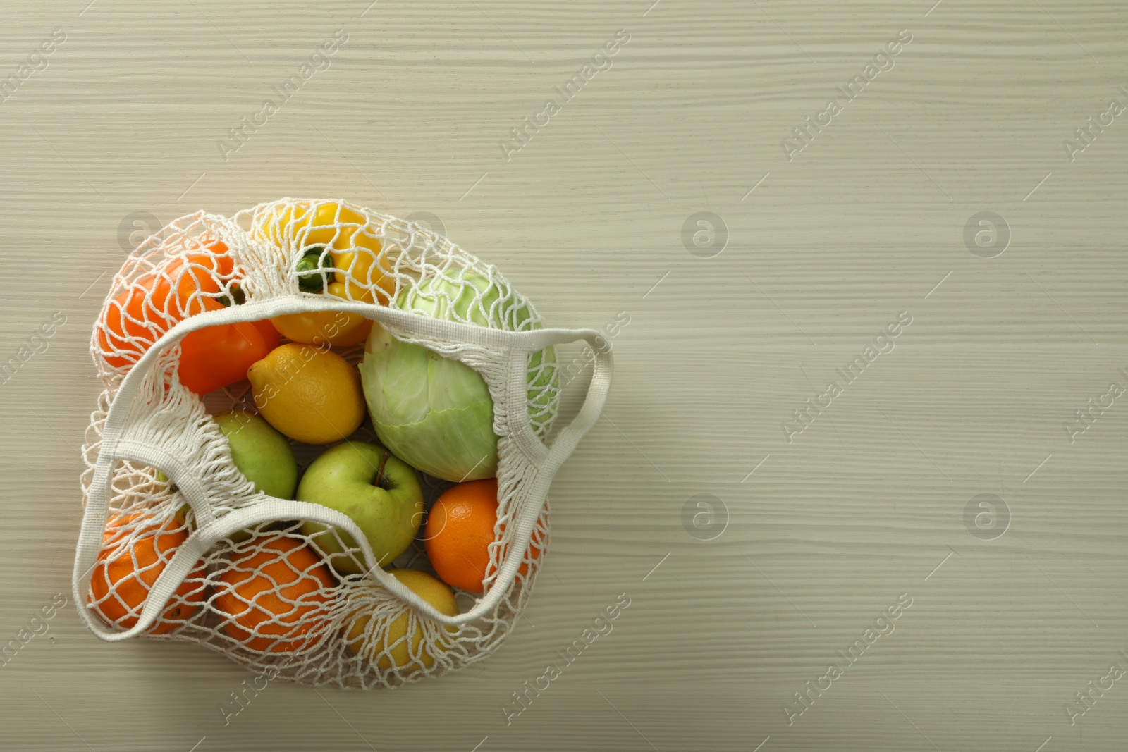 Photo of Net bag with vegetables and fruits on wooden table, top view. Space for text