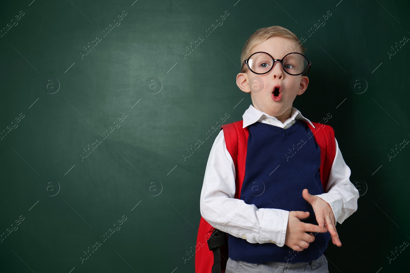 Photo of Cute little child wearing glasses near chalkboard, space for text. First time at school