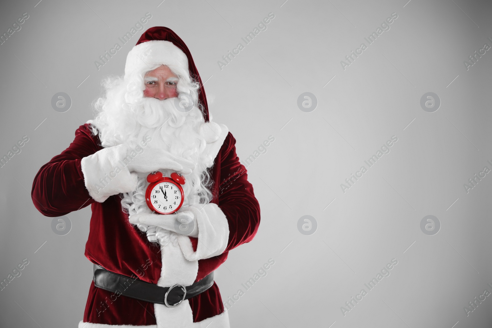 Photo of Santa Claus holding alarm clock on light grey background, space for text. Christmas countdown