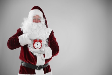 Santa Claus holding alarm clock on light grey background, space for text. Christmas countdown