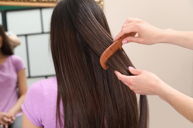 Photo of Woman combing friend's hair indoors, closeup view