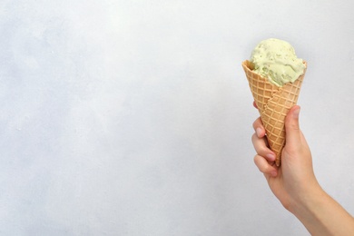 Woman holding waffle cone with delicious ice cream on light background, closeup. Space for text