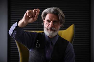 Photo of Psychotherapist with pendulum in office. Hypnotherapy session