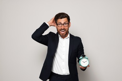 Emotional bearded man with alarm clock on light grey background. Being late concept