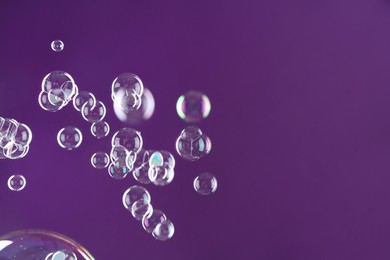 Photo of Beautiful transparent soap bubbles on purple background, space for text