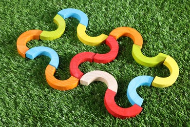 Photo of Colorful wooden pieces of play set on green grass, closeup. Educational toy for motor skills development