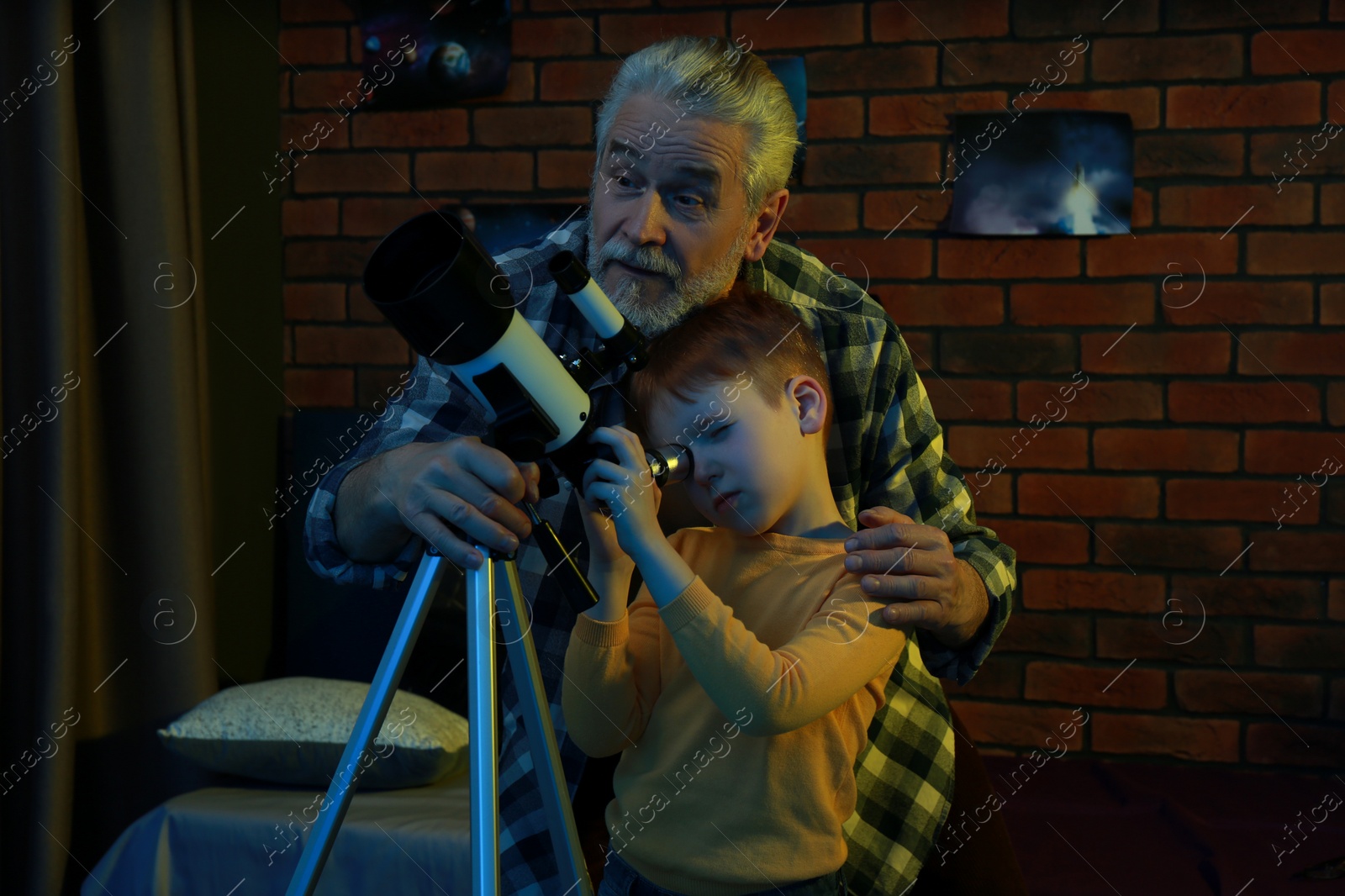 Photo of Little boy with his grandfather looking at stars through telescope in room