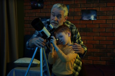 Photo of Little boy with his grandfather looking at stars through telescope in room