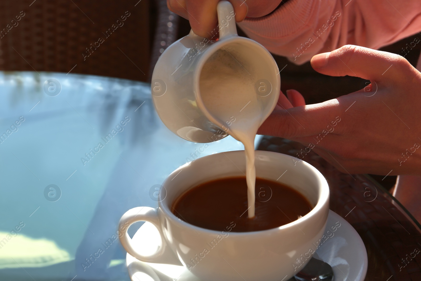 Photo of Woman pouring milk in coffee at table in cafe