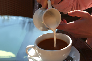 Photo of Woman pouring milk in coffee at table in cafe