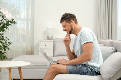 Photo of Happy man using laptop on sofa at home. Internet shopping