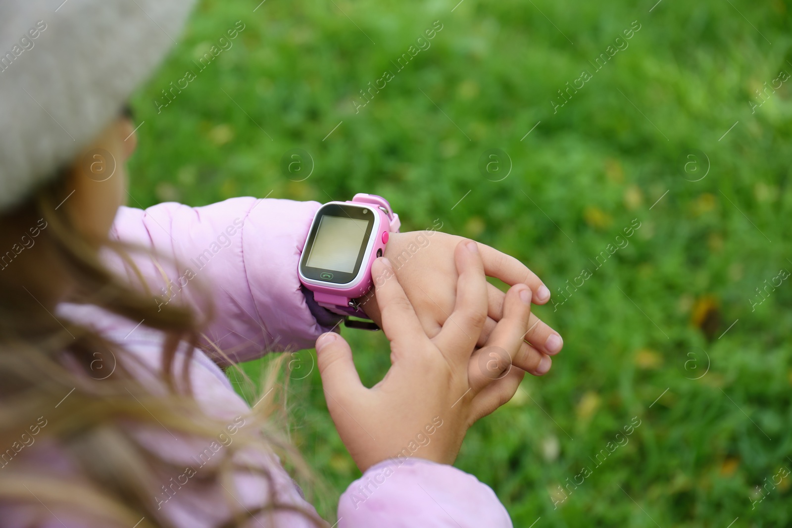 Photo of Little girl using smart watch outdoors, closeup