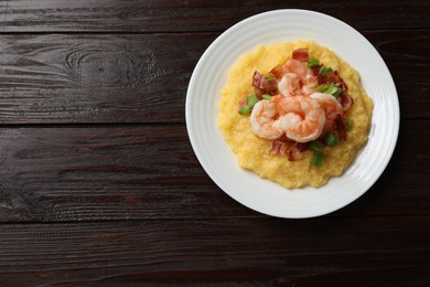 Photo of Plate with fresh tasty shrimps, bacon, grits and green onion on dark wooden table, top view. Space for text