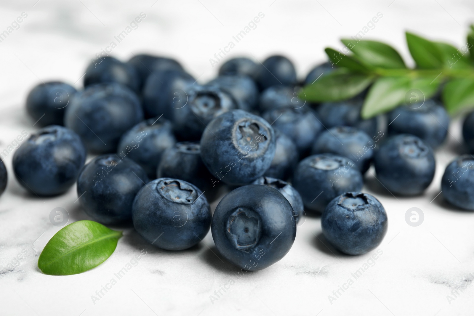 Photo of Pile of tasty fresh blueberries and leaves on light table, closeup