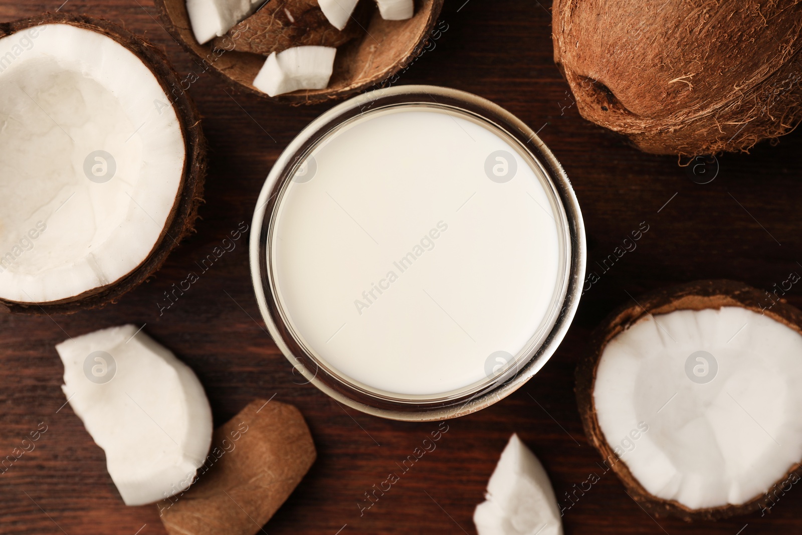 Photo of Glass o delicious vegan milk and coconut pieces on wooden table, flat lay